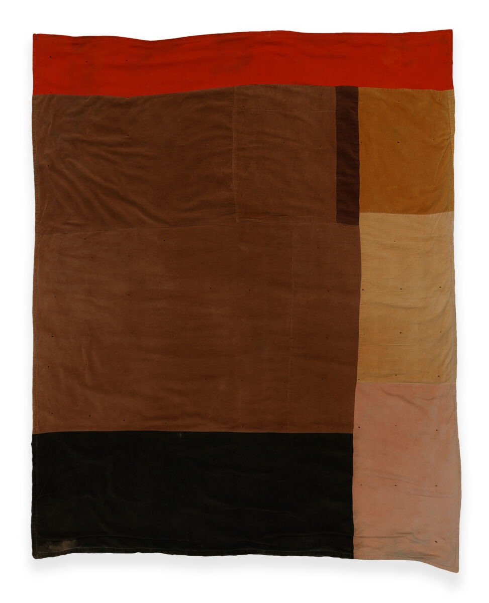 Quilt with a red stripe across the top and different sized squares in various earth tones beneath.